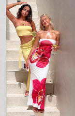 Two girls posing against a staircase in the sun. Brunette girl is wearing a yellow maxi dress and starfish necklace. Blonde girl is wearing a white maxi dress with a floral print.