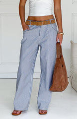 Model wears blue and white striped pants with a white top- brown belt- and matching handbag- showcasing stylish wide-leg trousers.