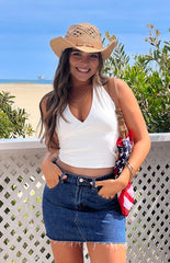 model wearing a white halter neck top wth cross over details at the bust paired with a mid wash denim mini skirt