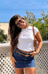 Model wearing a white baby tee with a USA graphic paired with a mid wash denim mini skirt