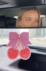 Two cherries with a bow air freshener on car review mirror.