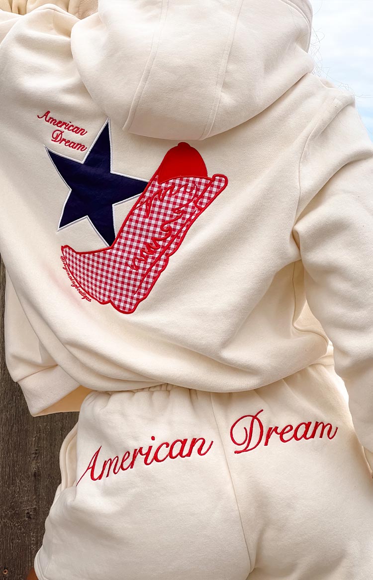 girl wearing a cream coloured hoodie with an emboidered red gingham cowboy boot and navy star on the back