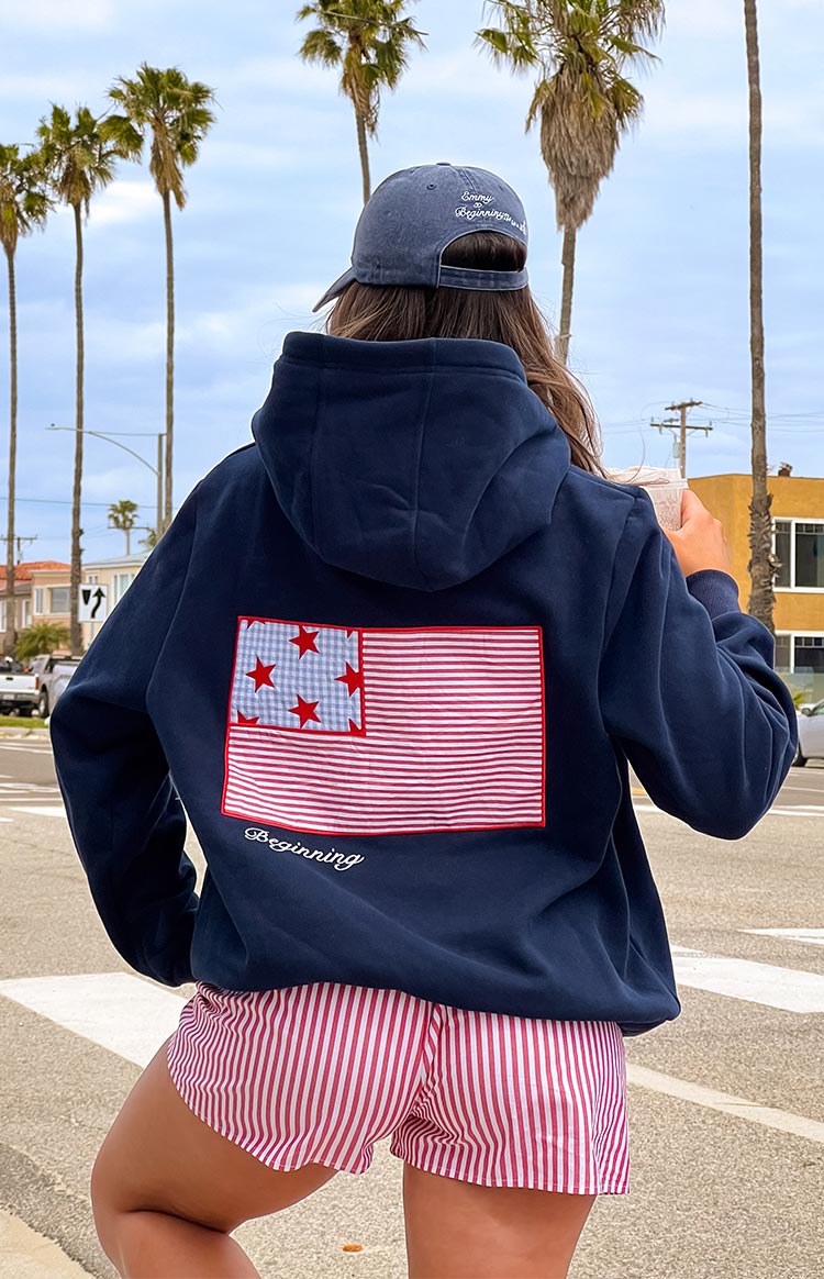 Girl wearing a navy sweatshirt with a red and blue embroidered flag on the back- paired with red and white striped shorts