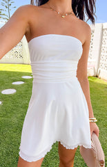 Close up photo of model wearing a white strapless mini dress. Model is wearing a gold necklace and bangles, and holding a woven handbag.
