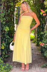blonde model wearing a yellow strapless maxi dress, yellow scarf, gold bracelet and nude heels holding a white woven handbag