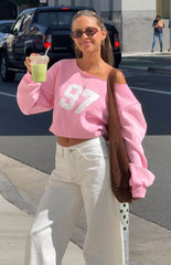 Woman sporting a trendy pink 97 off-shoulder sweatshirt and white wide-leg jeans for a comfy Spring style