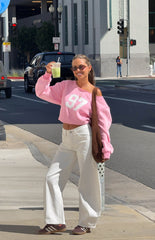 Woman sporting a trendy pink 97 off-shoulder sweatshirt and white wide-leg jeans for a comfy Spring style