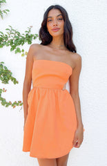 Model posing against white wall in orange strapless mini dress