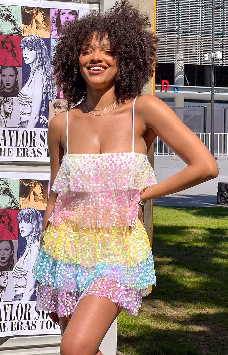 Girl smiling in a rainbow sparkle mini dress with her hand on her hip.