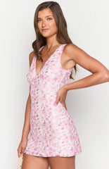 Brunette model wearing a pink floral lace mini dress and gold jewellery.