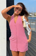 Model is wearing a red and white gingham halter-neck mini dress that buttons down the front. She carries a cream shoulder bag with a white and blue polka dot scarf tied to it.