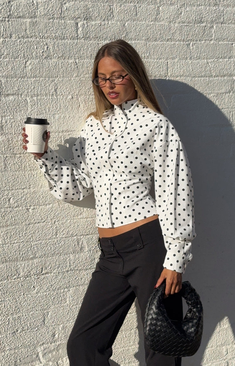 Woman in a trendy white polka dot high-neck jacket and black trousers a professional yet stylish look for work or events