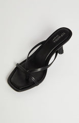 A single black heeled sandal with thin straps is shown on a light background. The sandal has a square toe and a small