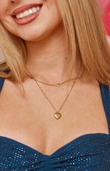 A layered gold-toned necklace set featuring a shorter chain with small delicate charms and a longer chain with a polished puffed heart pendant.
