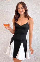 brunette model wearing a black and white contrast mini dress, gold bracelet and necklace holding a drink