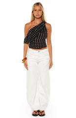 Model in a black polka dot asymmetrical top styled with white wide-leg jeans a perfect trendy outfit for a Summer evening