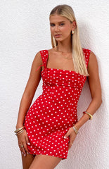 Blonde model wearing a red polka dot mini dress with ribbons at the straps and gathered bust details