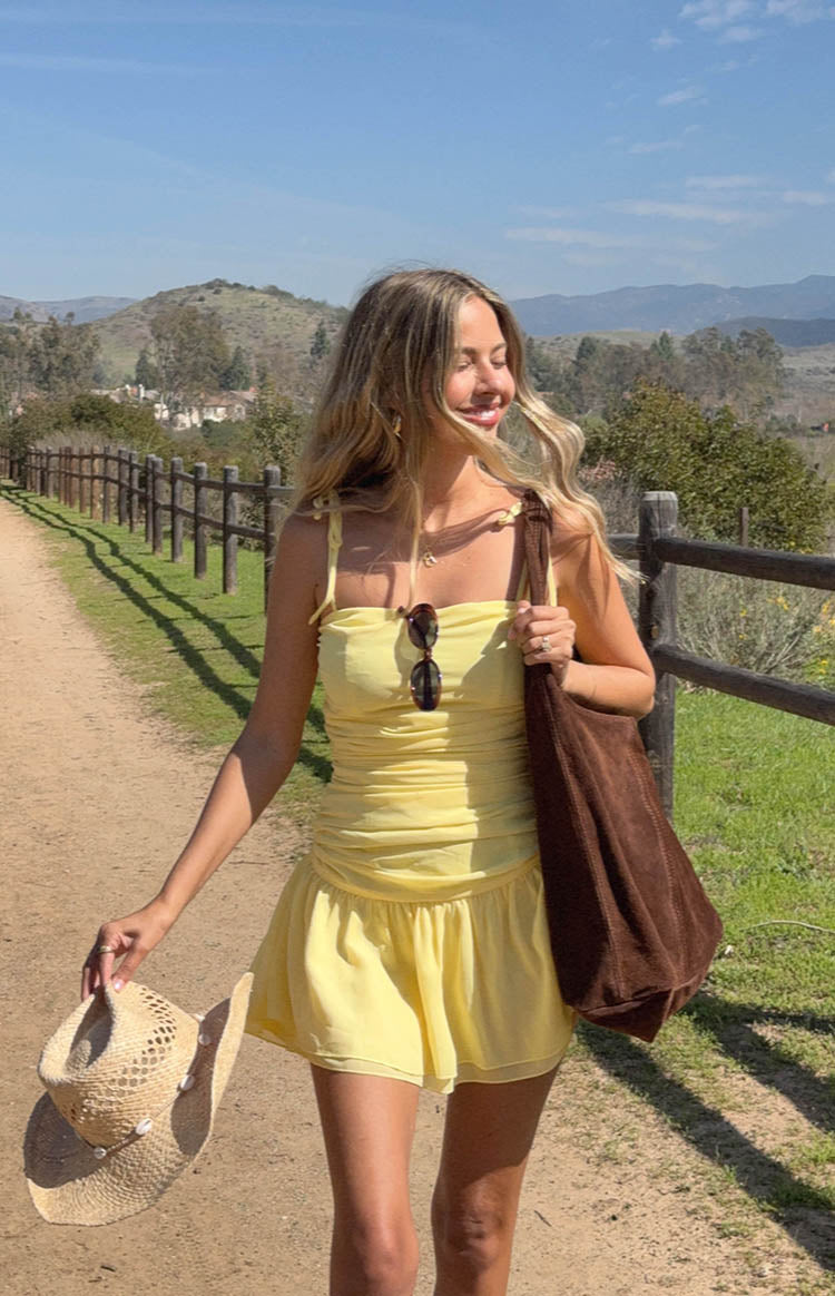 model wearing a yellow chiffon mini dress with ruched and ruffle skirt details