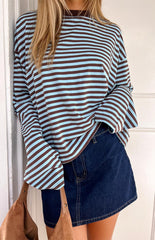 A person with long blonde hair models a blue and brown horizontally striped long-sleeved shirt and a dark blue denim mini skirt. A brown suede shoulder bag is slung over their left shoulder.
