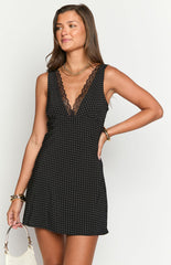 Model wearing a black mini dress with white polka dots and a black lace-trimmed V-neckline- accessorized with gold bangles.