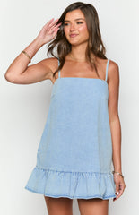 Brunette girl wearing a mid wash denim mini dress standing in front of a white wall.