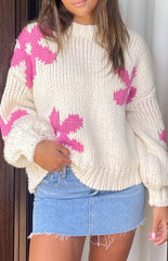 Model is posing and wearing a thick cream crochet sweater with pink floral designs. She is wearing a blue mini skirt.