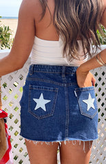 Girl wearing a dark wash denim mini skirt with white contrast stars on the back pockets- styled with a basic white top