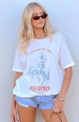 blonde model wearing a white oversized graphic tee with denim shorts styled with black sunglasses and gold jewellery