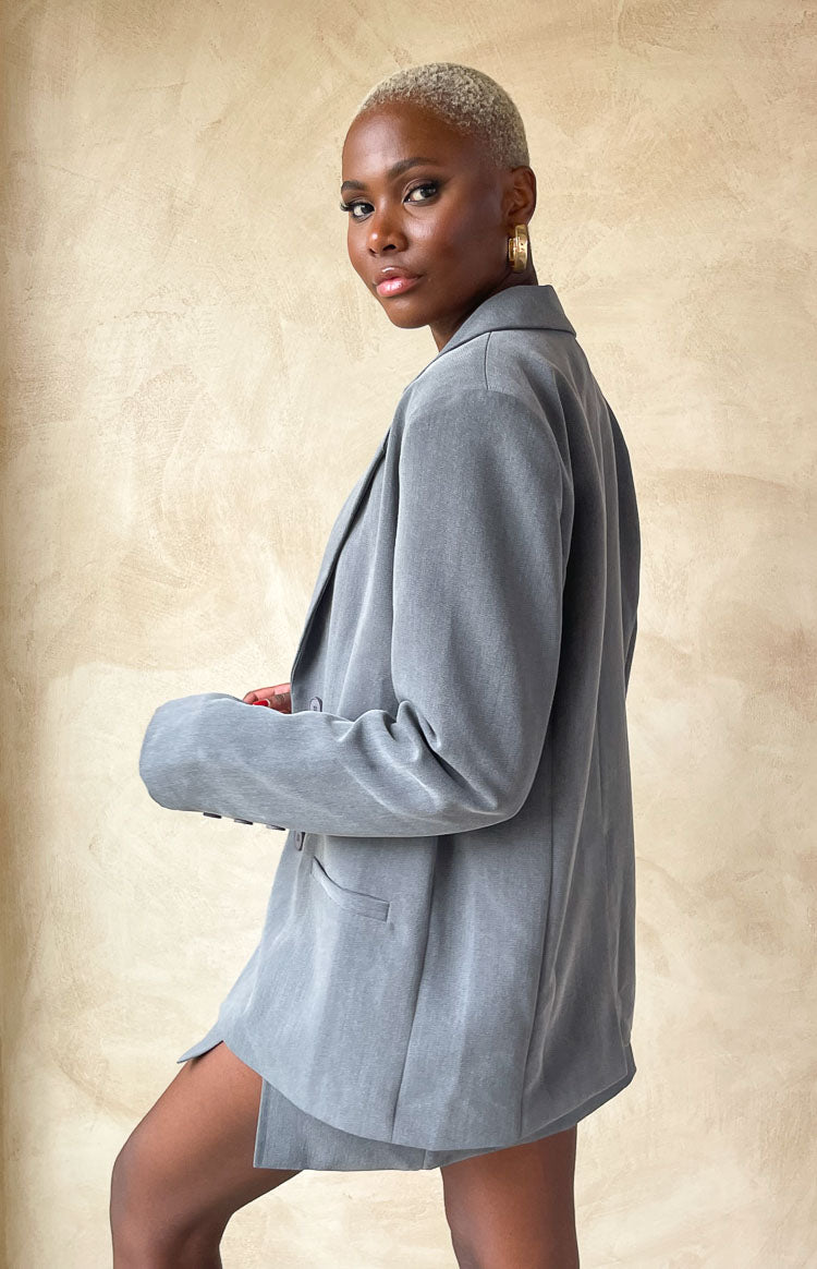 Grey Oversized Blazer, Model posing in front of beige wall in a side on stance.