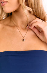 A model wears a fine gold chain necklace with a single red heart pendant. A lovely jewellery piece for a birthday gift or anniversary present. The delicate chain sits on the collarbone.