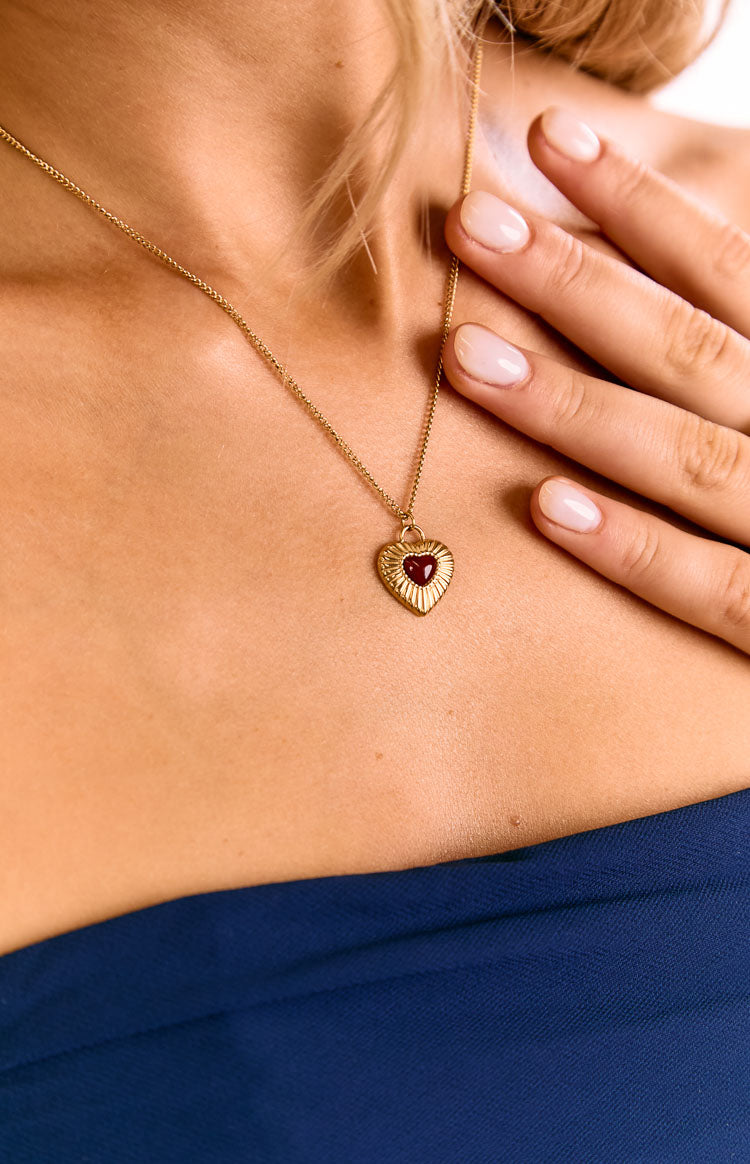 A model wears a fine gold chain necklace with a single red heart pendant. A lovely jewellery piece for a birthday gift or anniversary present. The delicate chain sits on the collarbone.