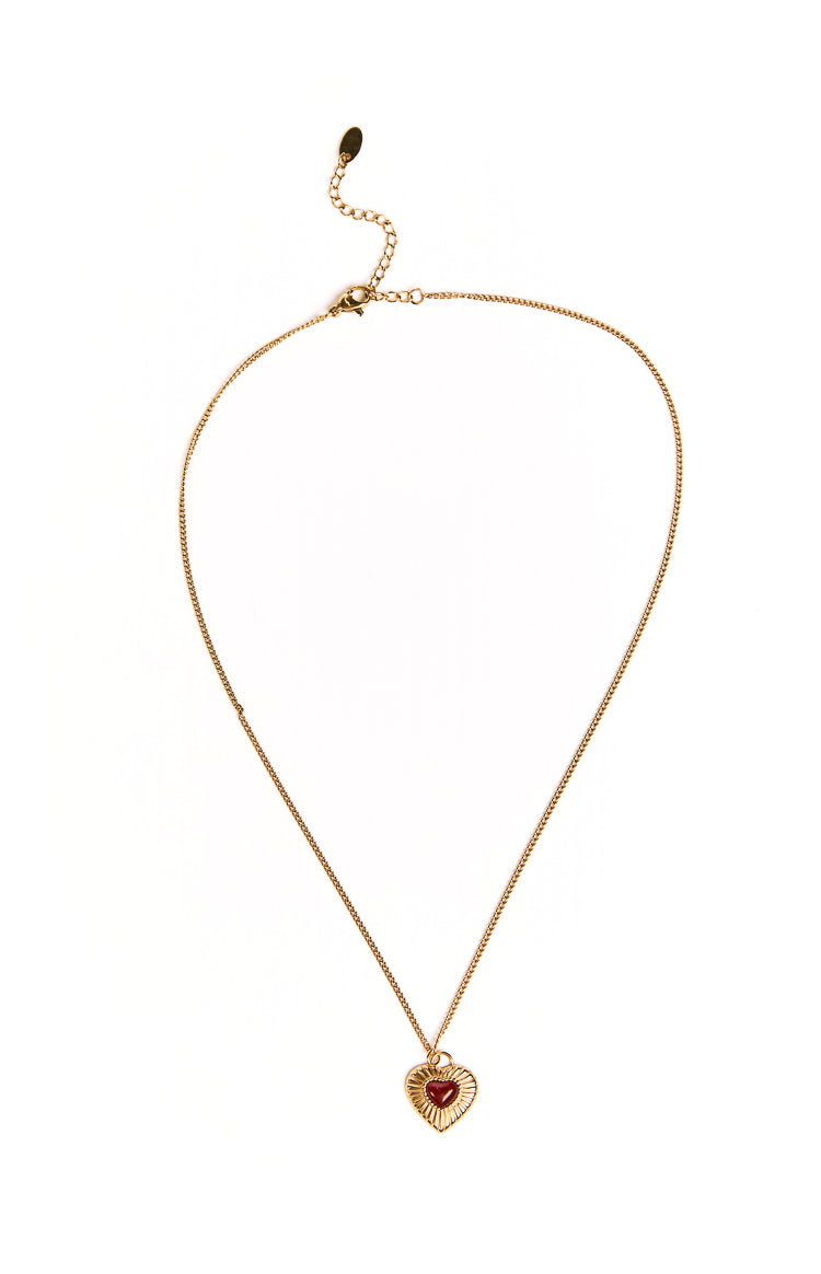 A delicate gold necklace featuring a single red heart pendant. This simple accessory elevates a casual weekend outfit or a special date night look. The pendant has a bright polished finish.