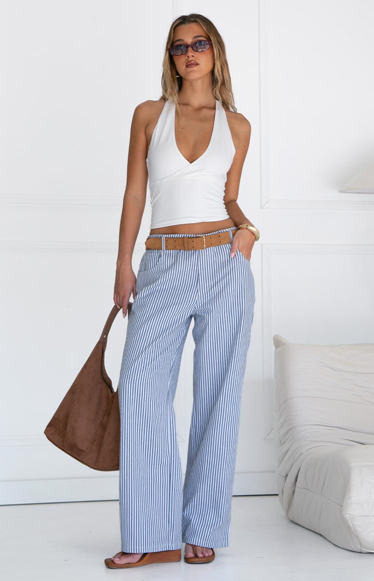 Model wears blue and white striped pants with a white top- brown belt- and matching handbag- showcasing stylish wide-leg trousers.