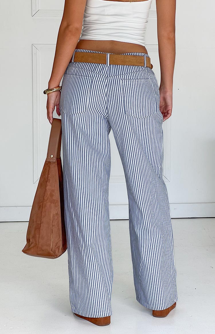 Model wears blue and white striped pants with a white top- brown belt- and matching handbag- showcasing stylish wide-leg trousers.