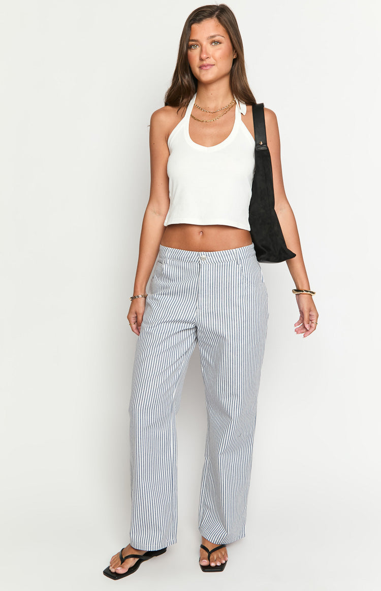 Model wears blue and white striped pants with a white top- brown belt- and matching handbag- showcasing stylish wide-leg trousers.