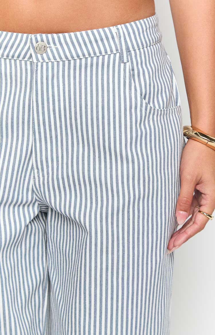 Model wears blue and white striped pants with a white top- brown belt- and matching handbag- showcasing stylish wide-leg trousers.