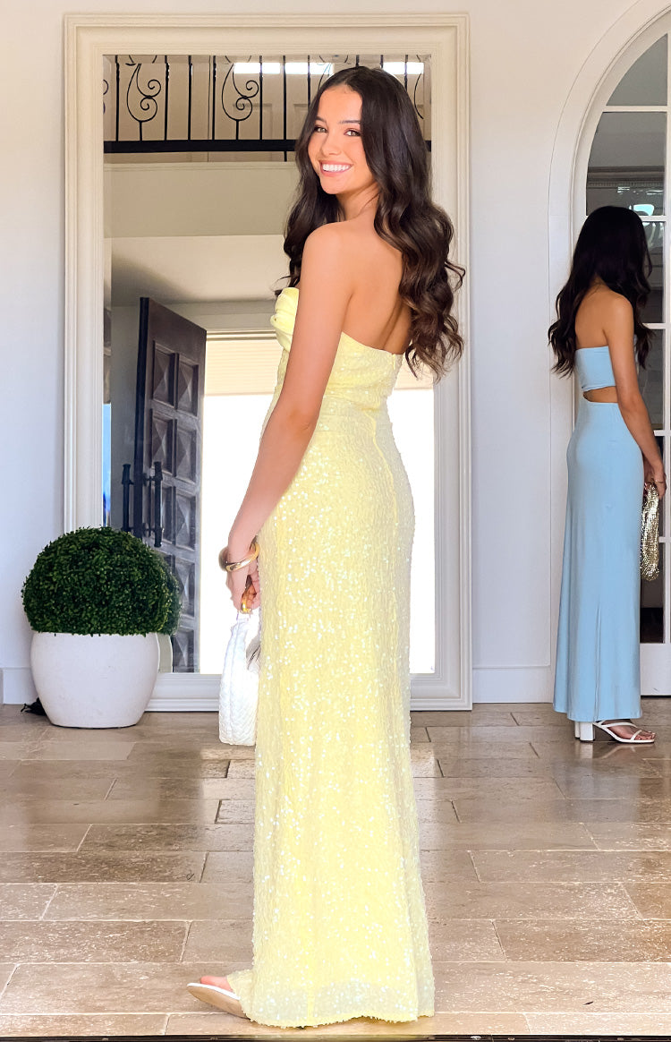 Girl smiling over her shoulder in a floor-length yellow sequin formal dress. The picture shows the side view- highlighting the strapless- fitted silhouette of the prom gown.