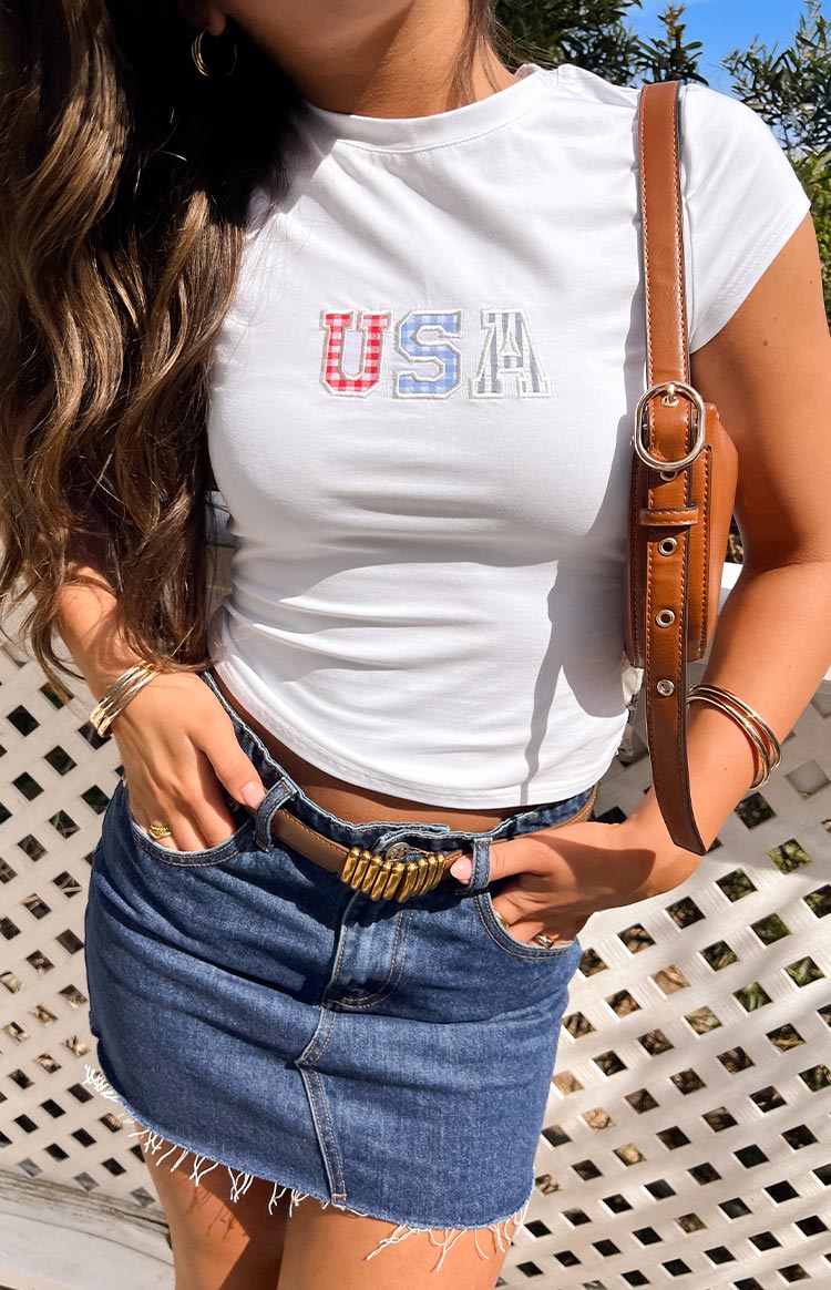 Girl wearing a white cropped t shirt with a USA embroidered design paired with a denim mini skirt