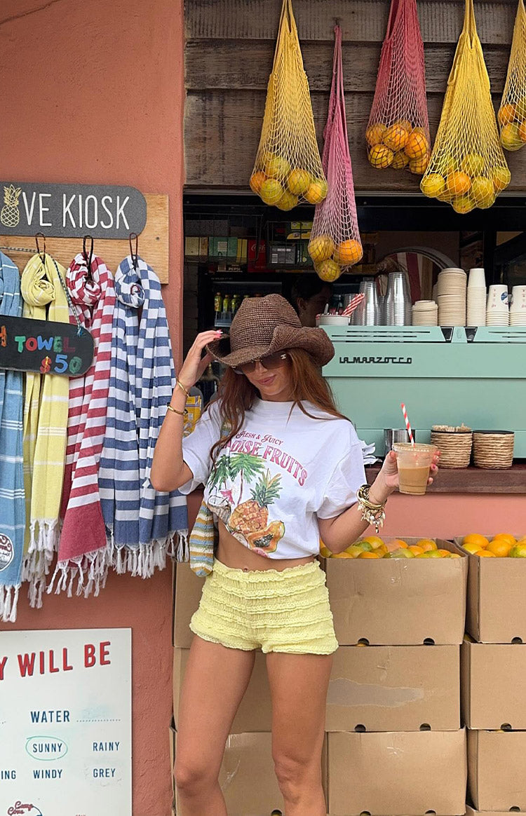 a white t-shirt with a tropical print is worn by a girl with jean shorts and a gold bracelet