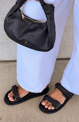 Girl wearing light blue denim jeans and black braided sandals and holding a black handbag.
