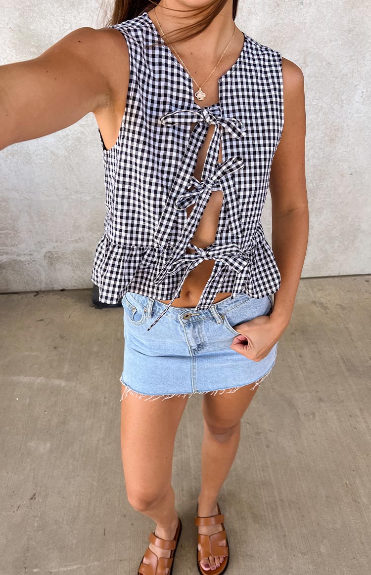 A black and white gingham print sleeveless top with a V-neckline- multiple tie-front details- and a ruffled peplum hem- paired with a light wash denim mini skirt.