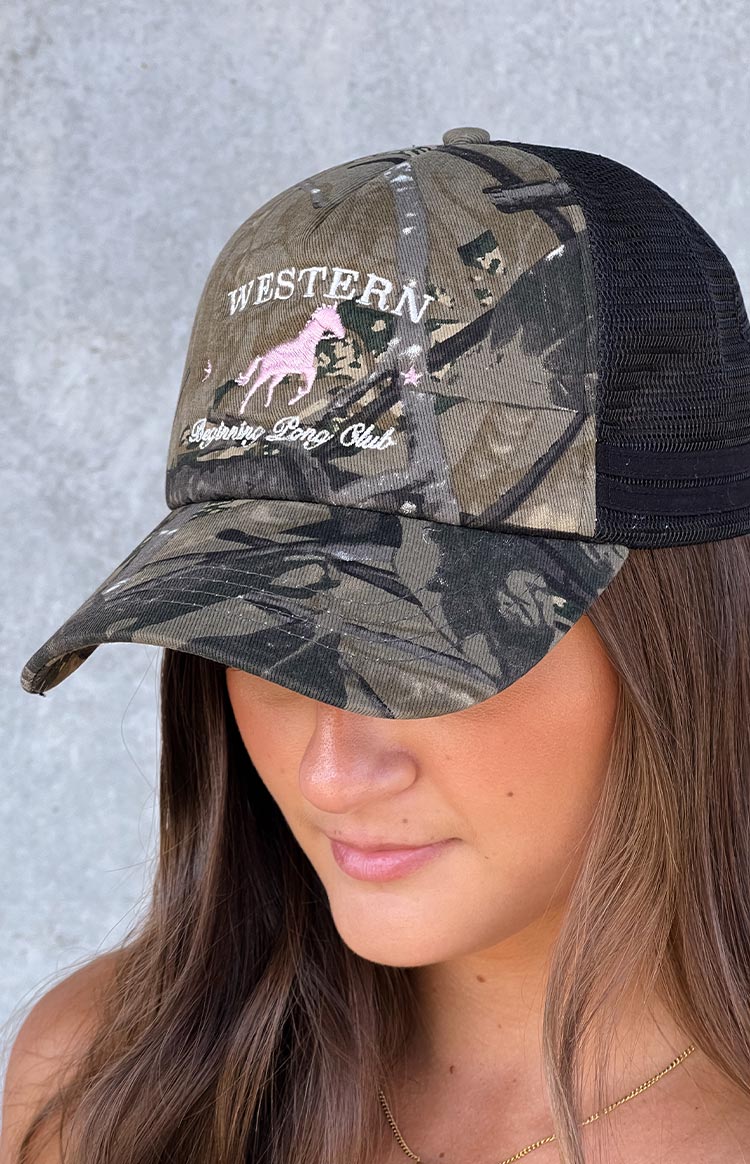 Model wearing a green and brown camo printed trucker hat with a pink pony embroidered graphic