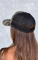 Model wearing a green and brown camo printed trucker hat with a pink pony embroidered graphic