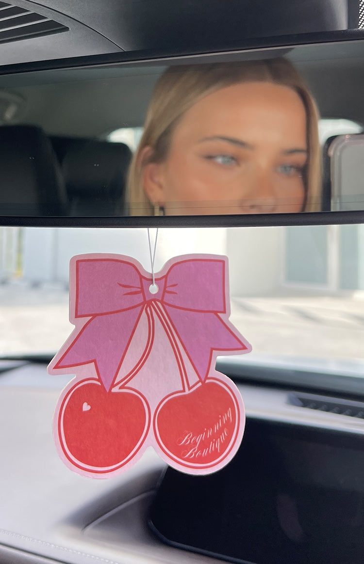 Two cherries with a bow air freshener on car review mirror.