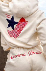 girl wearing a cream coloured hoodie with an emboidered red gingham cowboy boot and navy star on the back