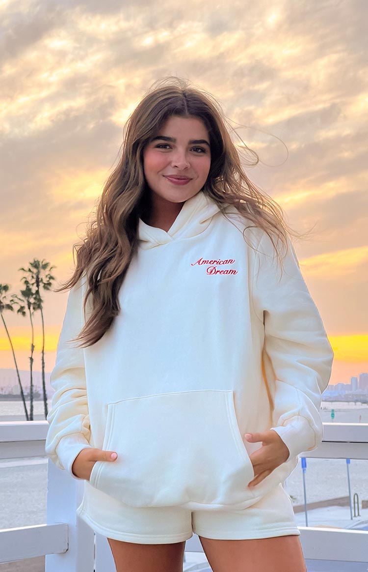 model wearing a cream coloured sweater with an embroidered text graphic on the front and an oversized front pocket