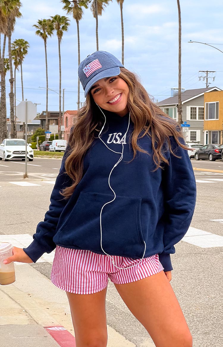 Girl wearing a navy sweatshirt with a red and blue embroidered flag on the back- paired with red and white striped shorts