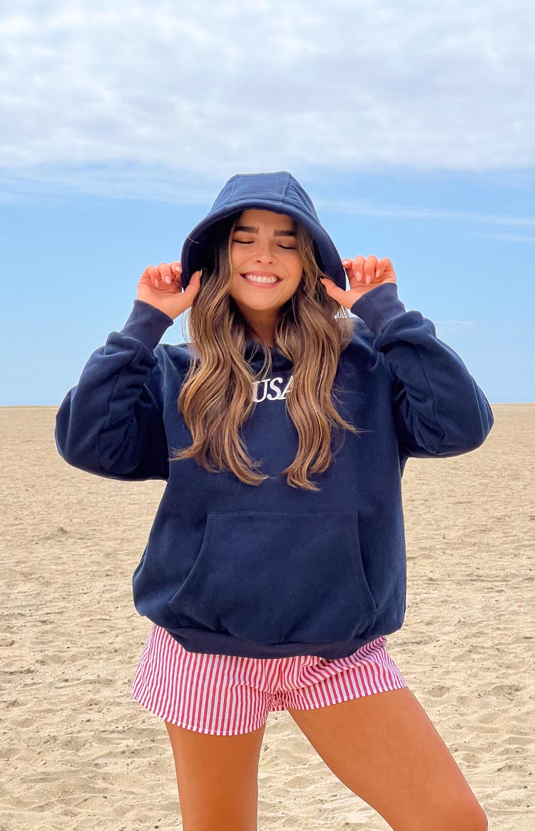 Girl wearing a navy sweatshirt with a red and blue embroidered flag on the back- paired with red and white striped shorts