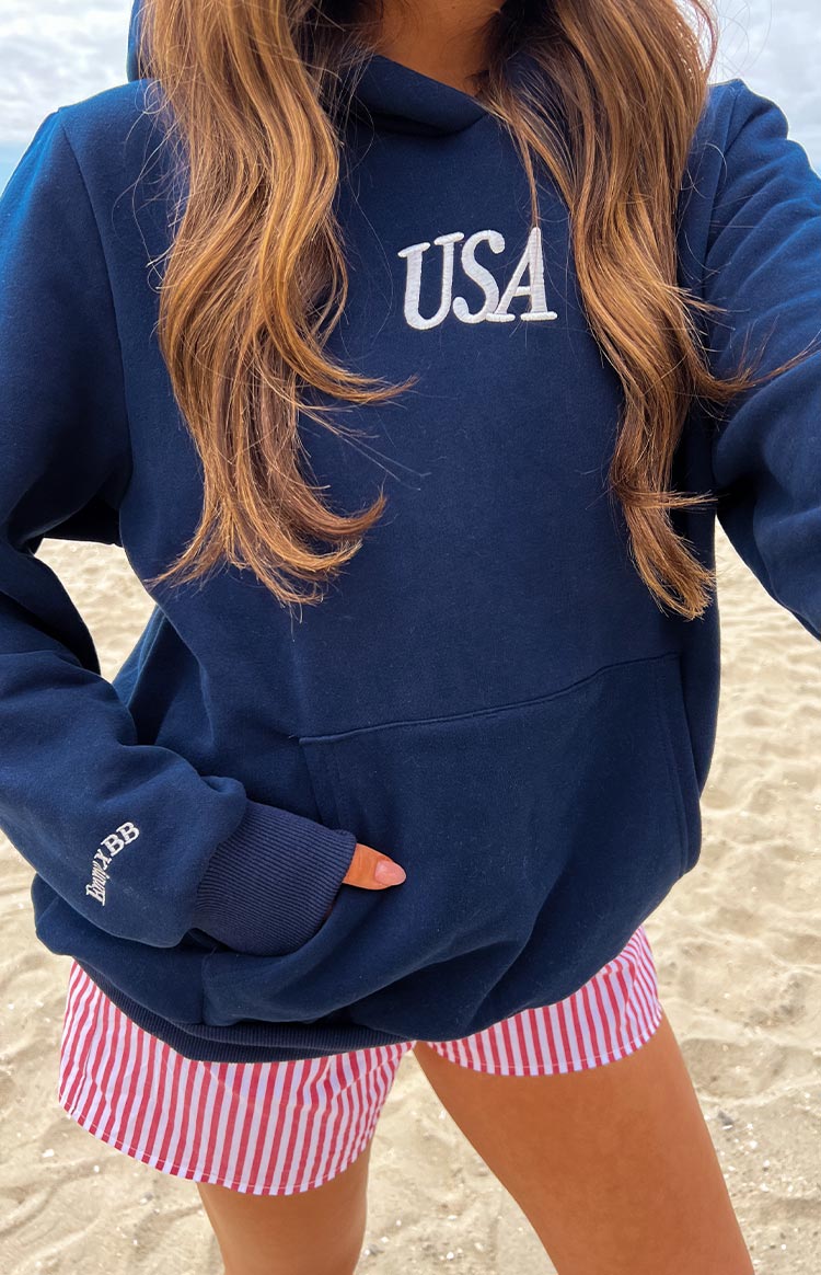 Girl wearing a navy sweatshirt with a red and blue embroidered flag on the back- paired with red and white striped shorts
