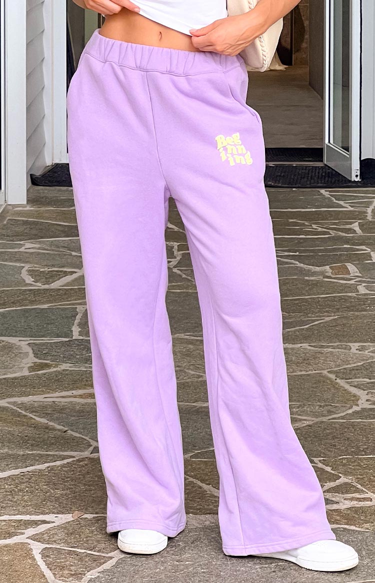 Model wearing purple tracksuit pants with white sneakers.